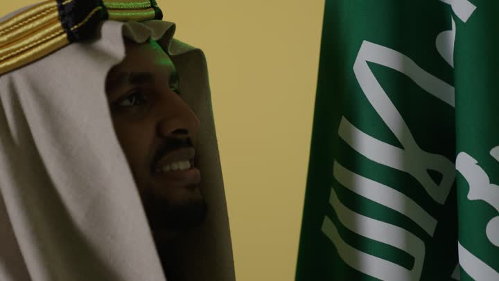 رجل سعودي بالزي التقليدي مع العلم الوطني