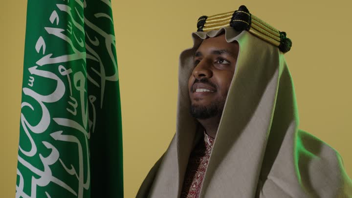 رجل سعودي بزي يوم التأسيس مع العلم الوطني السعودي