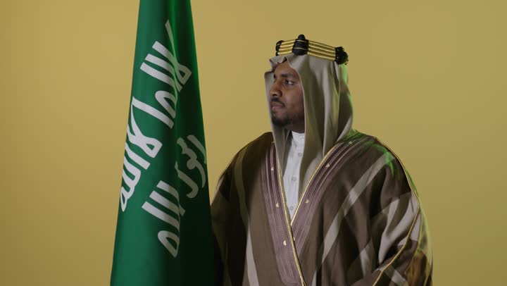 رجل سعودي بلباس يوم التأسيس مع العلم الوطني