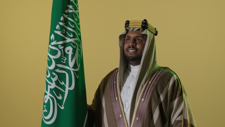 رجل سعودي بزي يوم التأسيس مع العلم الوطني السعودي