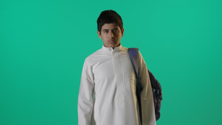 طالب سعودي بالثوب يرفع إبهامه أمام خلفية خضراء