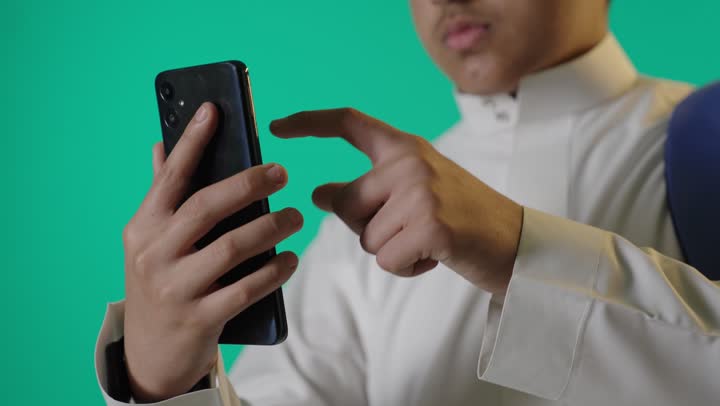 طالب سعودي يستخدم الهاتف الذكي أمام خلفية خضراء