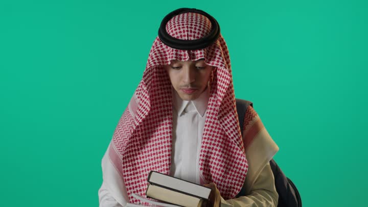 طالب سعودي يحمل كتباً أمام خلفية خضراء