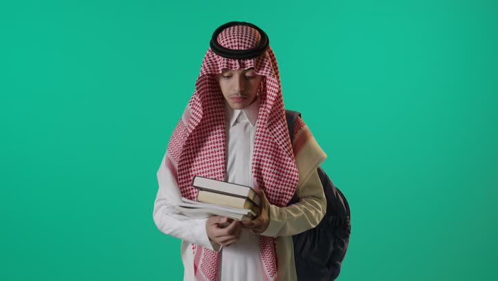 طالب سعودي يحمل كتباً أمام خلفية خضراء