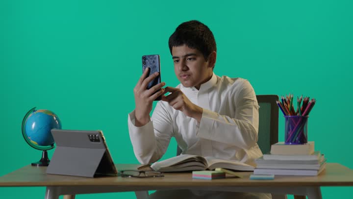 Saudi Boy Using Smartphone at Desk Green Screen