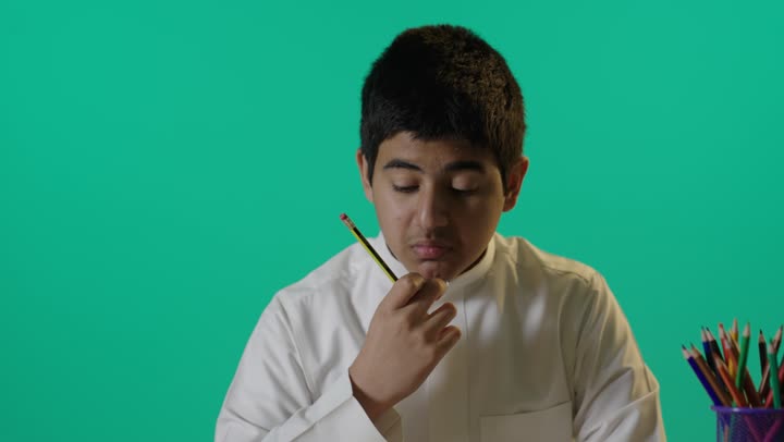 Saudi Student Boy Writing at Desk on Green Screen