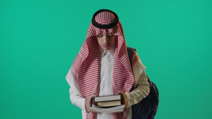 طالب سعودي يحمل كتباً أمام خلفية خضراء