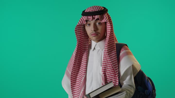 طالب سعودي يحمل كتباً أمام خلفية خضراء