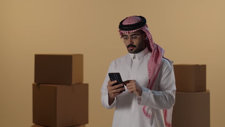 Saudi Man Using Smartphone Near Shipping Boxes