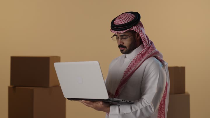 رجل سعودي يستخدم المحمول في مستودع مع صناديق