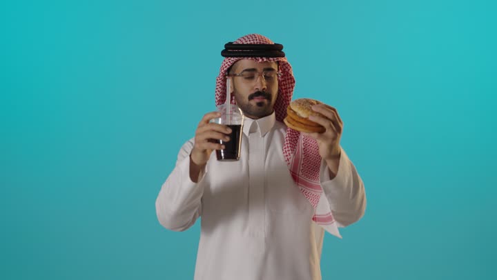 رجل سعودي يحمل برجر ومشروب غازي خلفية زرقاء