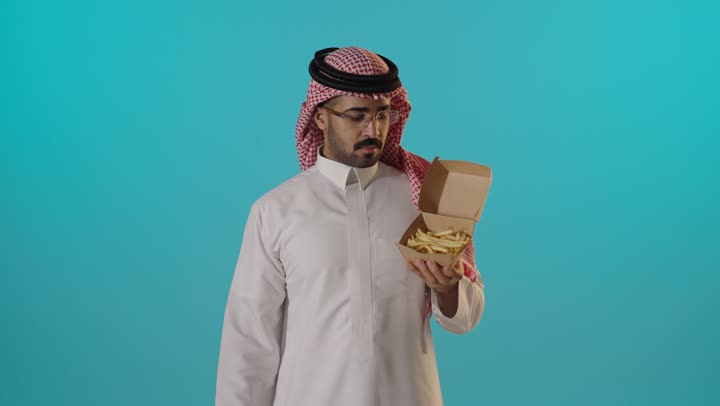 رجل سعودي يشير بالإبهام للأسفل تجاه البطاطس المقلية