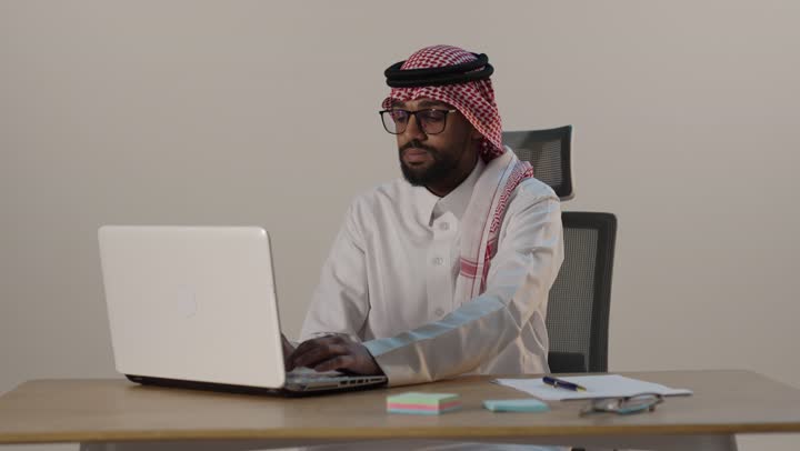 Saudi Businessman Working on Laptop and Writing Notes