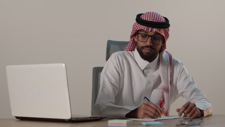 رجل أعمال سعودي يعمل على المحمول ويكتب في المكتب