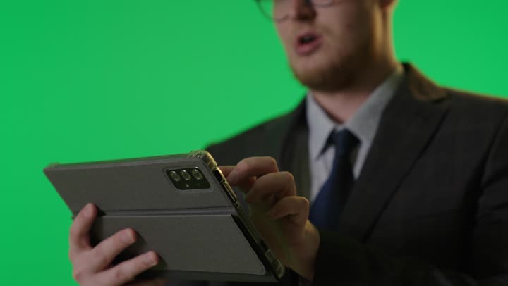 رجل أعمال أجنبي يستخدم جهاز لوحي أمام شاشة خضراء