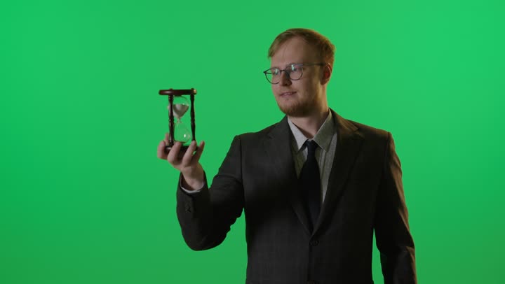 رجل أعمال يمسك ساعة رملية على خلفية كروما خضراء