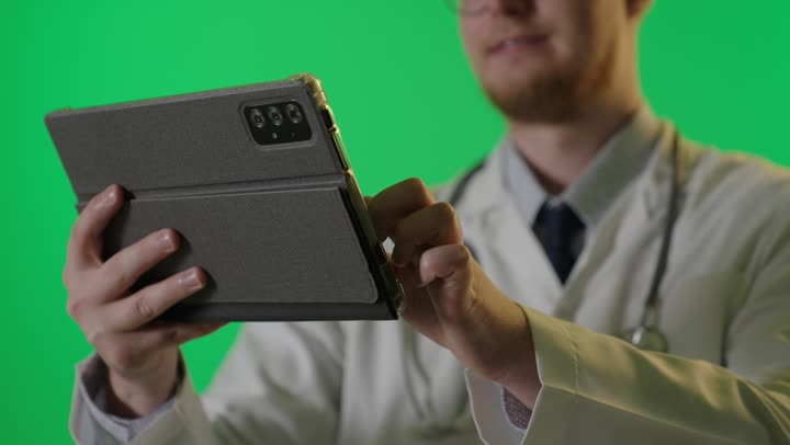 طبيب يستخدم جهاز لوحي أمام شاشة خضراء لقطة قريبة