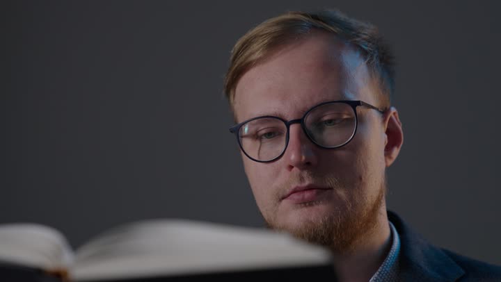 رجل قوقازي يرتدي نظارات يقرأ كتاباً في الداخل