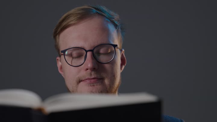 رجل يرتدي نظارات يقرأ كتاباً في استوديو مظلم