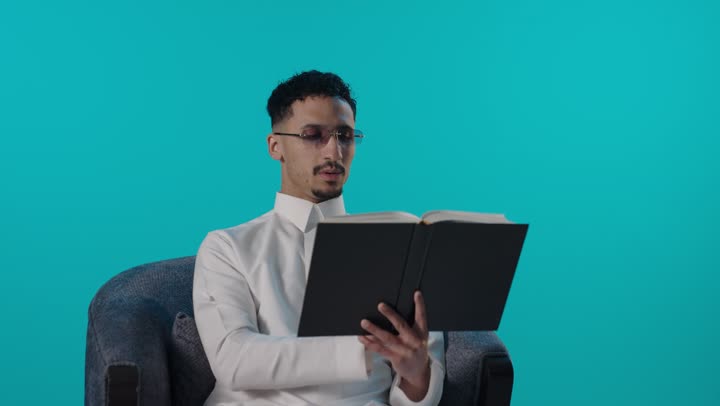 Saudi Man Reading Book in Studio Blue Background