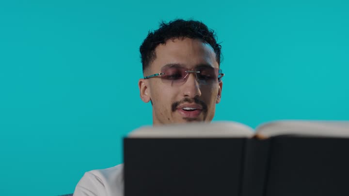 شاب عربي يقرأ كتاباً في استوديو بخلفية تركوازية زرقاء