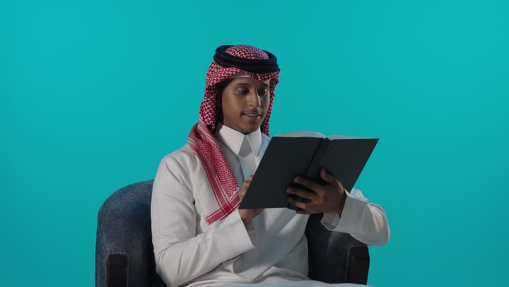 رجل سعودي يقرأ كتاباً في الاستوديو بخلفية زرقاء