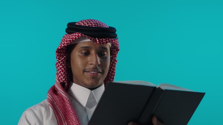 Saudi Man Reading Book on Blue Background Studio Shot