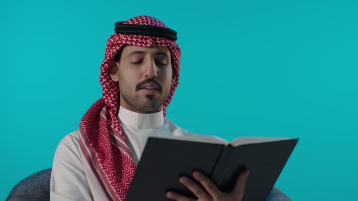 رجل سعودي يقرأ كتاباً في استوديو خلفية زرقاء فيديو
