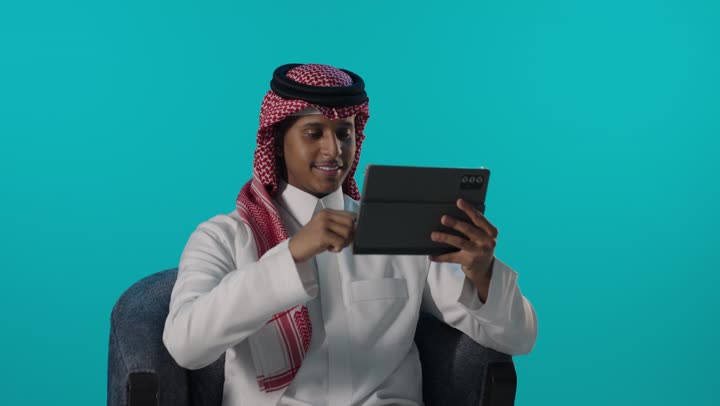 رجل سعودي يستخدم جهازاً لوحياً بخلفية فيروزية