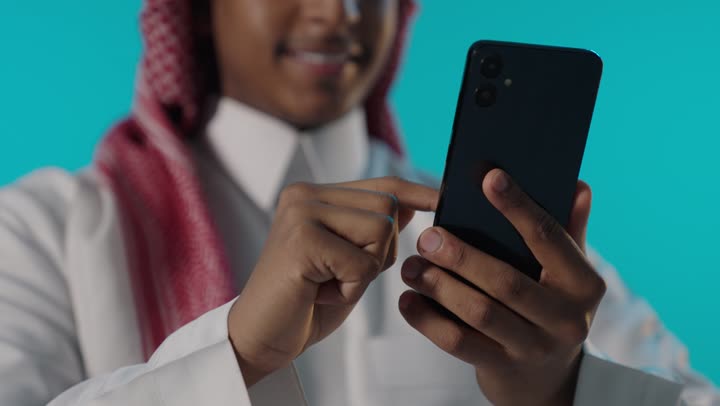 رجل سعودي يستخدم الهاتف الذكي على خلفية زرقاء