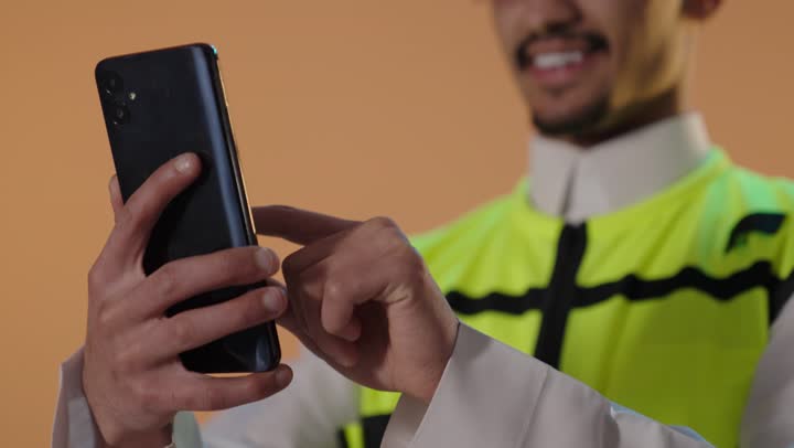 رجل سعودي يرتدي سترة سلامة يستخدم الهاتف الذكي