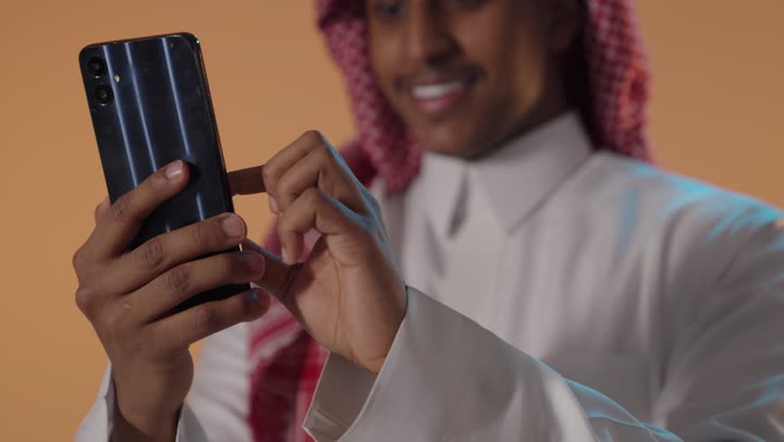 Saudi Man Using Smartphone on Orange Background