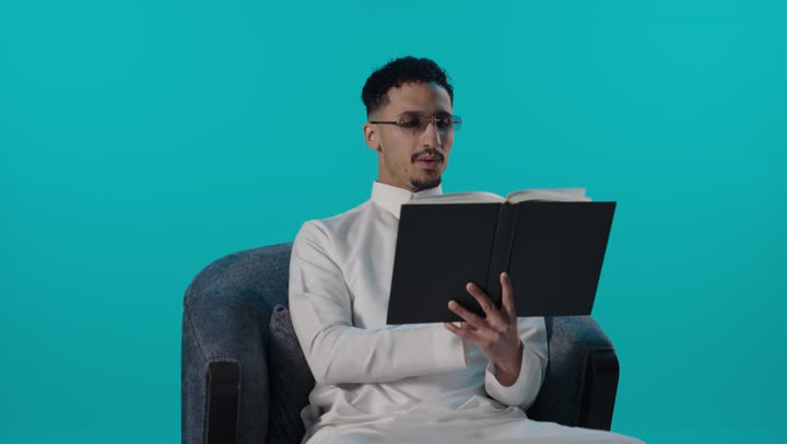 رجل سعودي بالثوب يقرأ كتاباً في الاستوديو