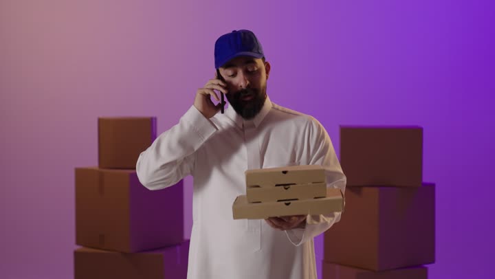 رجل توصيل سعودي يتحدث بالهاتف مع علب بيتزا
