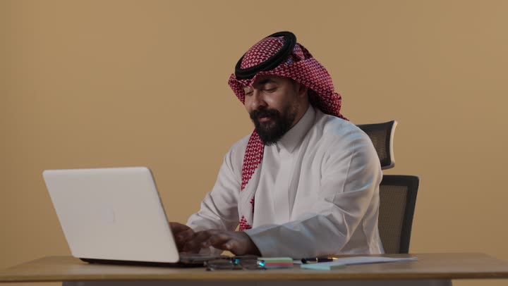 Saudi Businessman Working on Laptop and Writing Notes