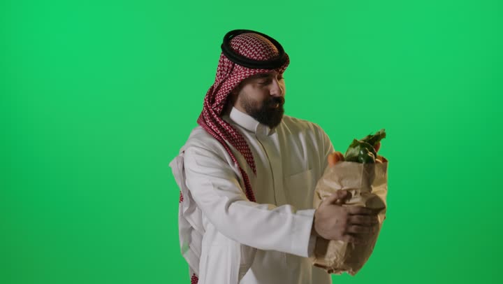 رجل سعودي يحمل كيس خضروات أمام شاشة خضراء