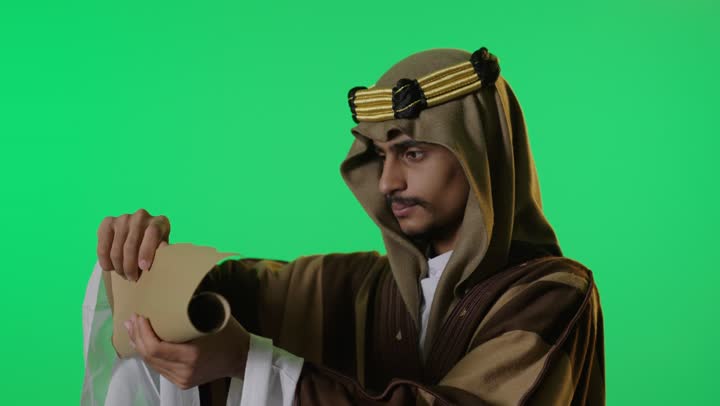 رجل سعودي بملابس يوم التأسيس يقرأ مخطوطة خلفية خضراء