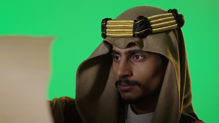 رجل سعودي بملابس يوم التأسيس يقرأ وثيقة خلفية خضراء