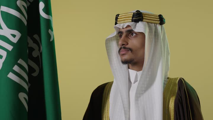 رجل سعودي بالزي التقليدي مع العلم السعودي