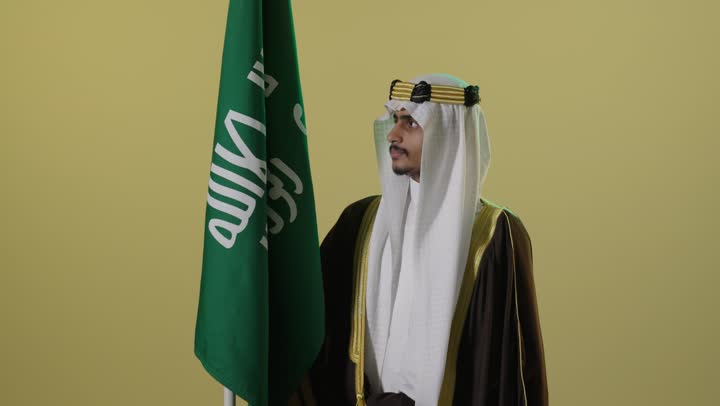 رجل سعودي بالزي التقليدي مع علم المملكة العربية السعودية