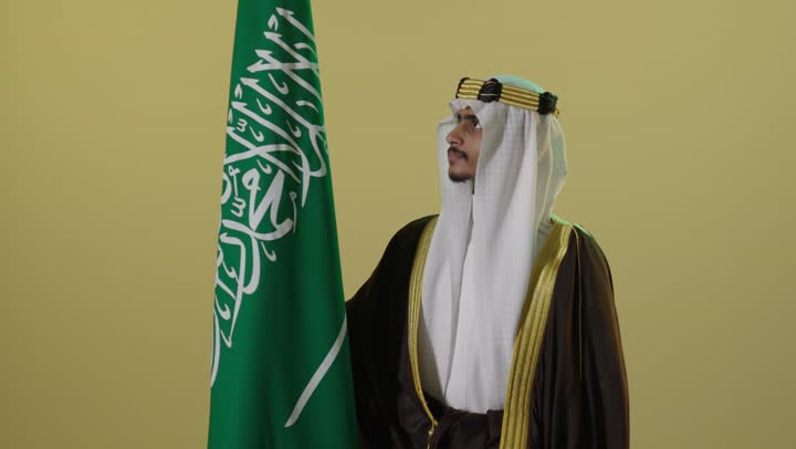 شاب سعودي بملابس يوم التأسيس التقليدية مع العلم