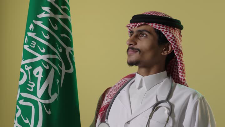 طبيب سعودي يقف بجانب العلم الوطني في يوم التأسيس