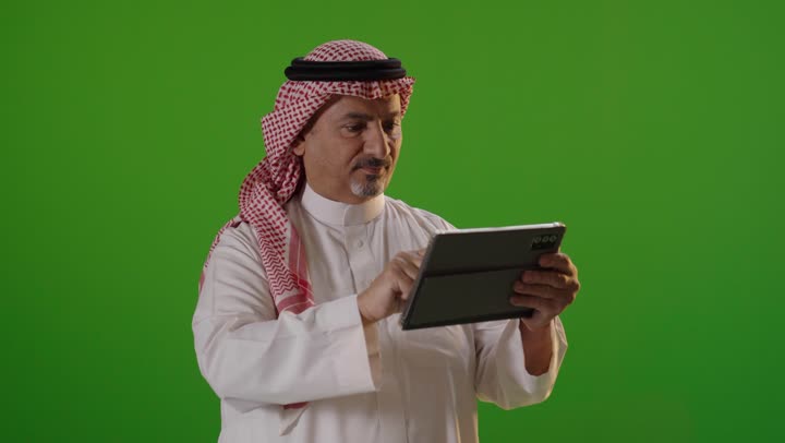 رجل سعودي يستخدم جهاز لوحي أمام خلفية خضراء