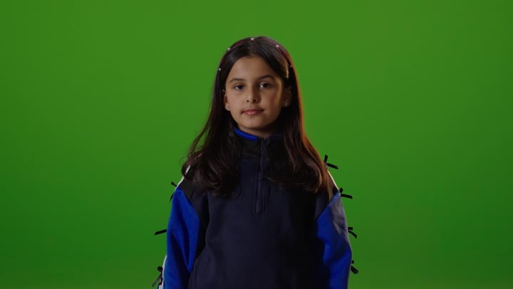 A Saudi Arabian Gulf girl wearing casual attire is looking at the camera and pointing her thumb up, a sign of admiration and satisfaction, with a green chroma background.