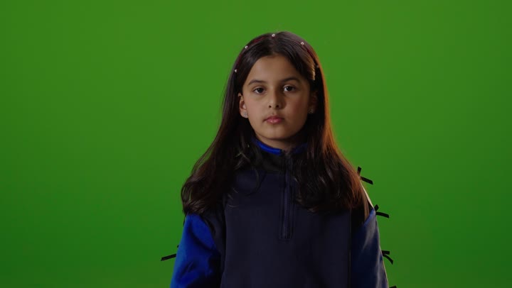 A Saudi Arabian Gulf girl wearing casual attire is looking at the camera and gesturing with her hand to ask for something to stop, with a green chroma background.