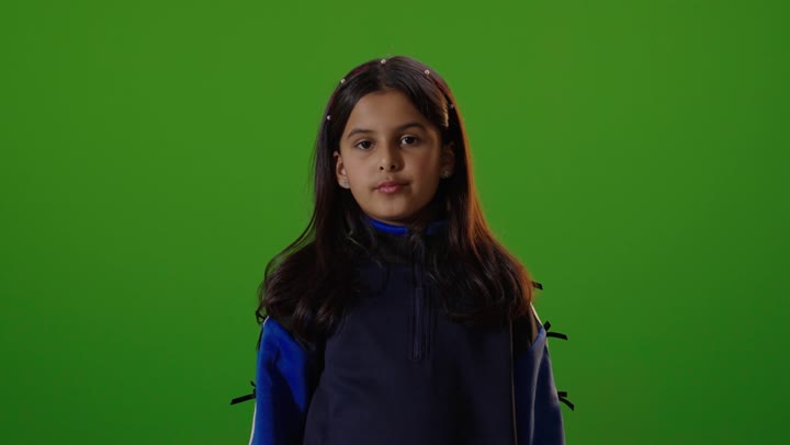 A Saudi Arabian Gulf girl wearing casual attire is looking at the camera and gesturing with her hand to ask for something to stop, with a green chroma background.
