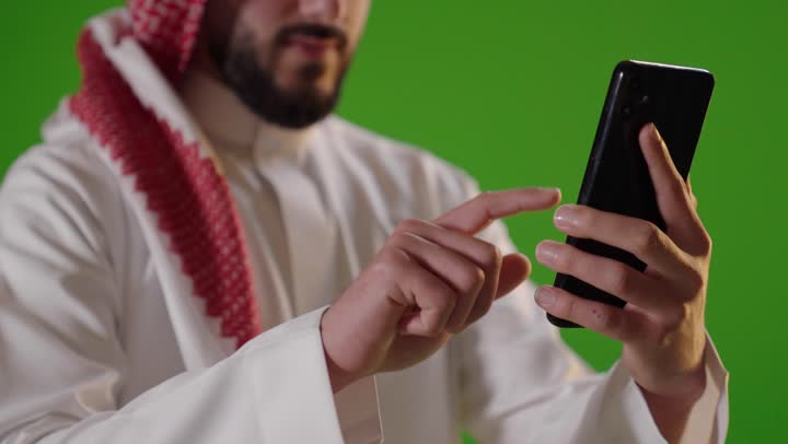 رجل سعودي يستخدم الهاتف الذكي على خلفية كروما خضراء