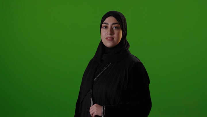امرأة سعودية بالعباءة تقف أمام شاشة خضراء