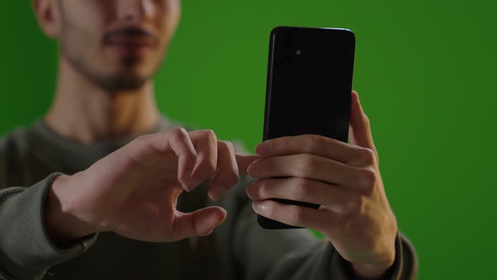 شاب يستخدم الهاتف الذكي بخلفية شاشة خضراء