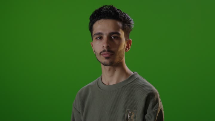 شاب عربي أمام كروما خضراء بوضعية تقاطع الذراعين